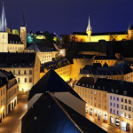 **

Prompt: A vibrant cityscape of Luxembourg, blending modern architecture with historic buildings. Focus on the illuminated night view of the old town, showcasing the blend of sophistication and history. Capture the charm of narrow streets and the panoramic views from the Bock Casemates.

**
